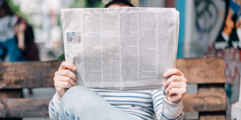 Man reading a Thinkific News newspaper on a bench