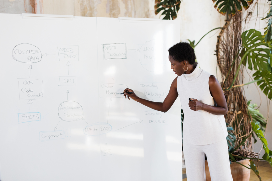 Woman with short hair drawing scheme on whiteboard during business conference in creative workplace